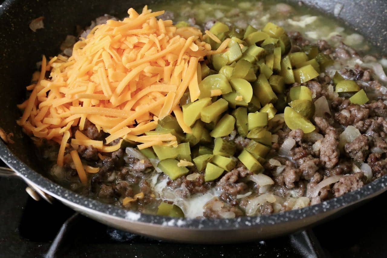 Add shredded cheddar cheese and chopped pickles to browned beef mixture.