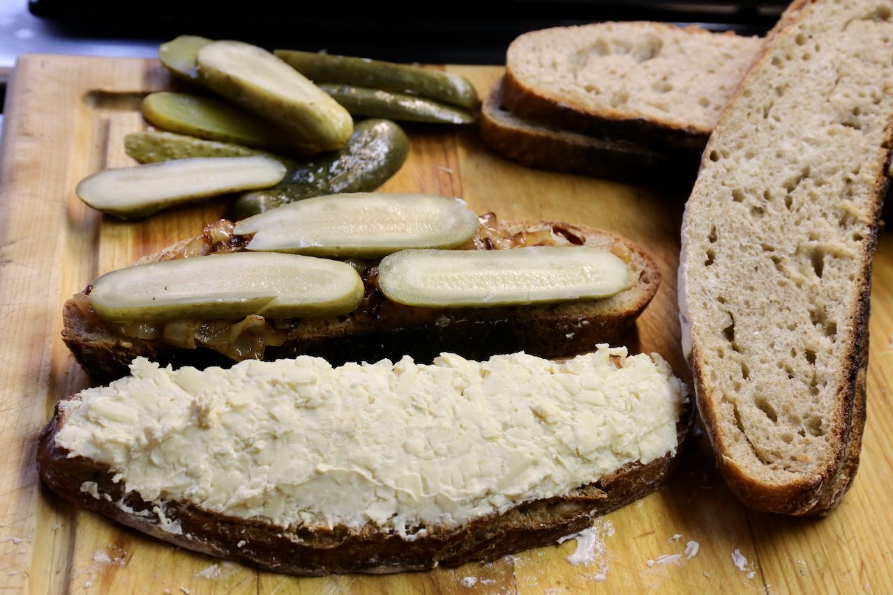 Schmear cheese mixture one one bread slice and caramelized onions and pickles on another.