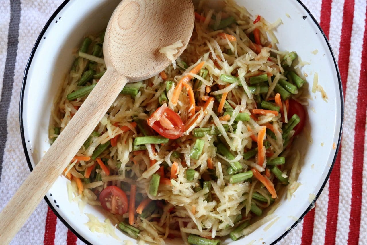 Stir Lao Papaya Salad ingredients with a wooden spoon in a large mixing bowl until fully combined.