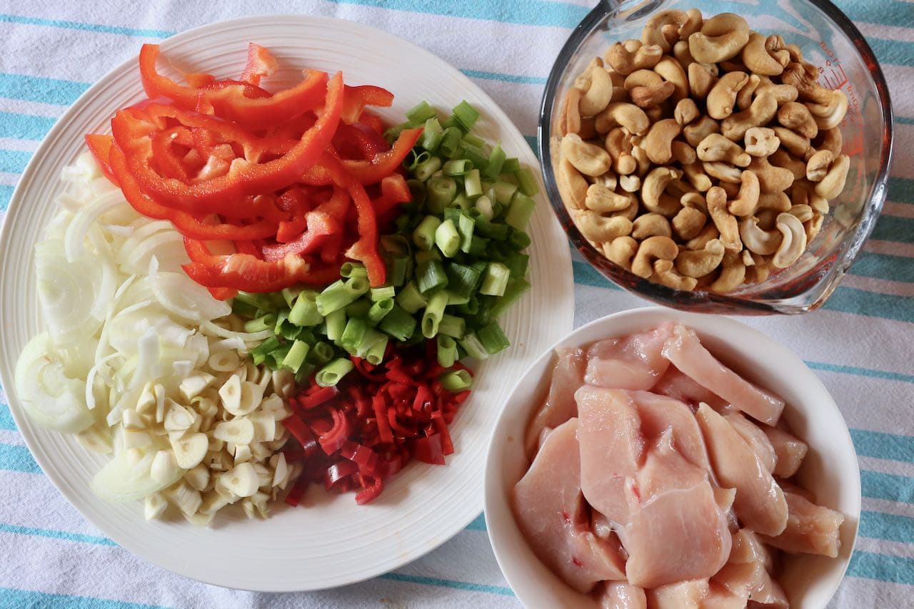 Prep Gai Pad Med Mamuang ingredients featuring sliced chicken, red pepper, scallions, onion, garlic and chili.