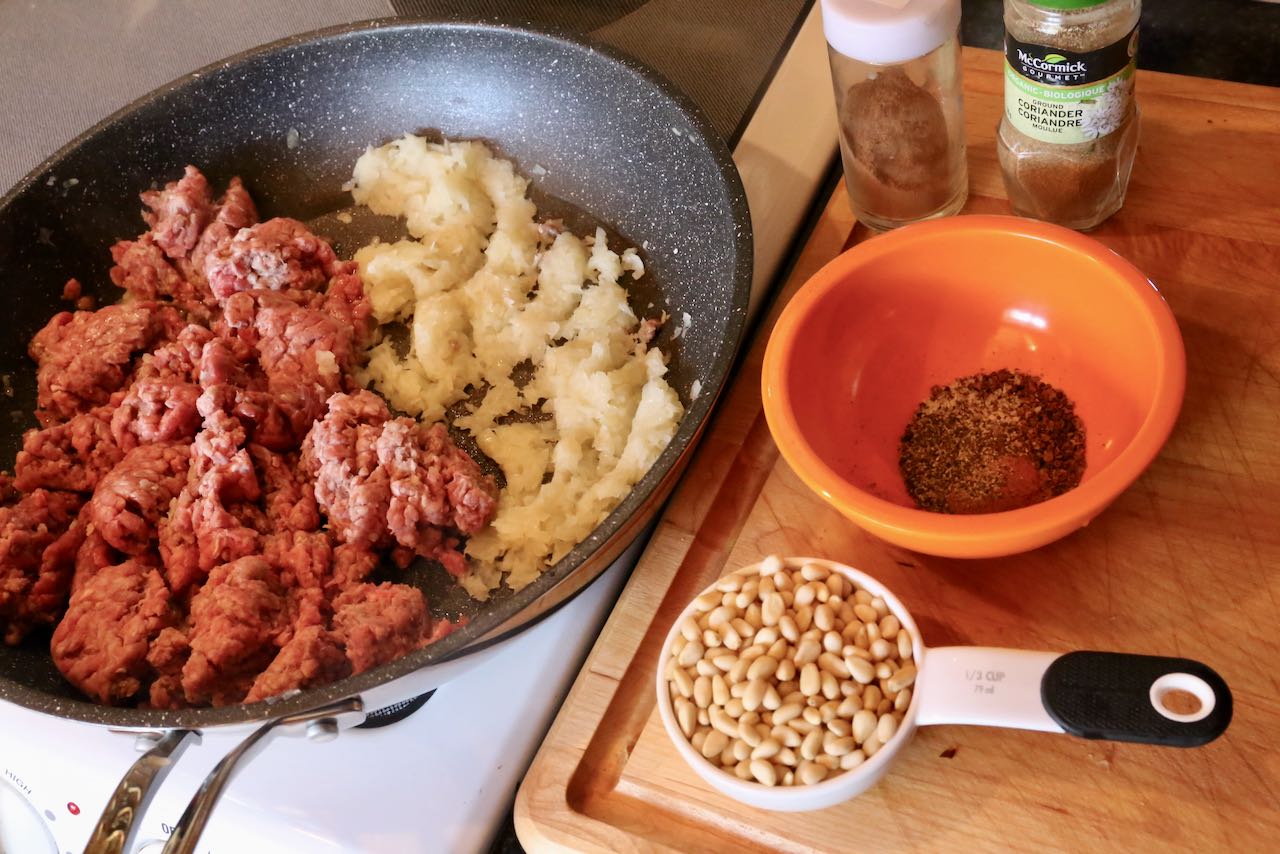 Prepare Lebanese Kibbeh filling by frying minced beef, onions, spices and pine nuts in a skillet.