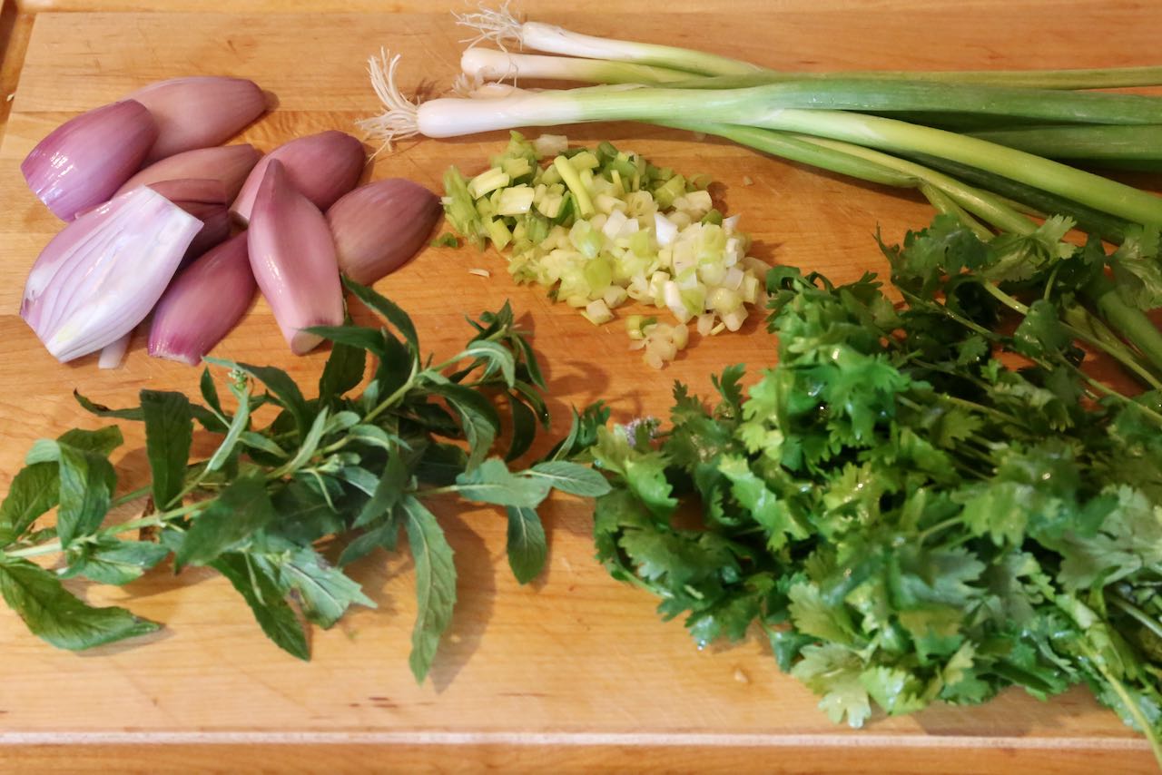 Begin Nam Tok preparation by slicing scallions, shallots, mint and cilantro.