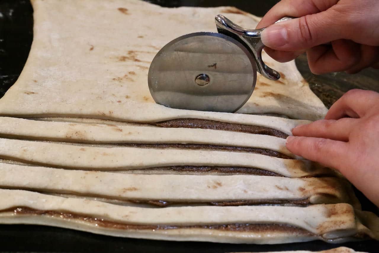 Use a pizza cutter to slice strips of Kardemummabullar dough.