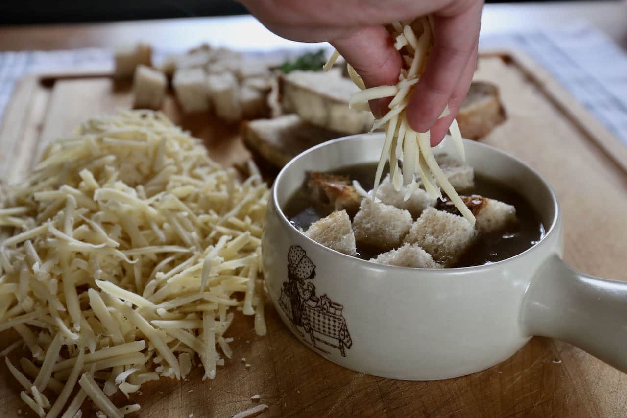 Top Vegetarian French Onion Soup with sourdough bread cubes and sprinkle with shredded Gruyere Cheese.