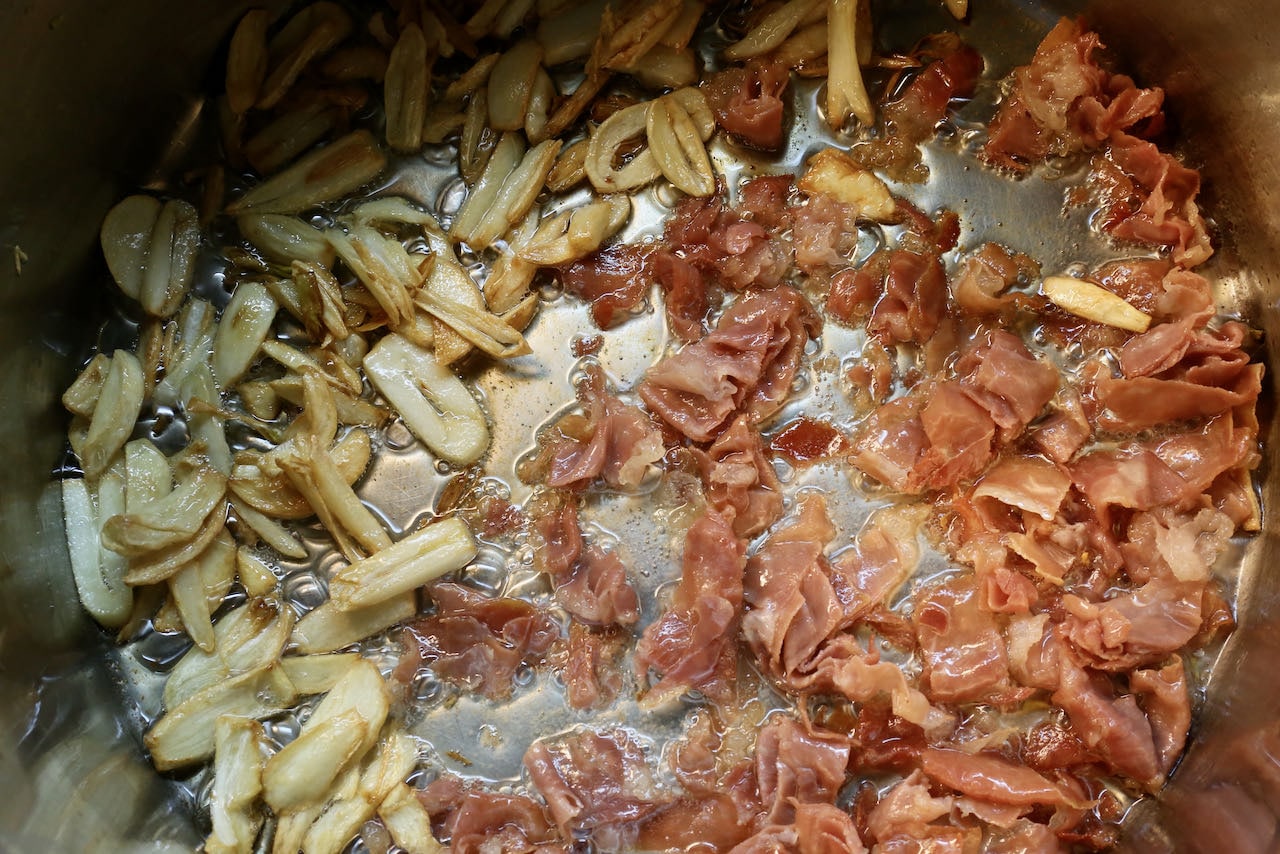 Begin preparing our Spanish Soup recipe by frying garlic and cured ham in a large pot with oil.