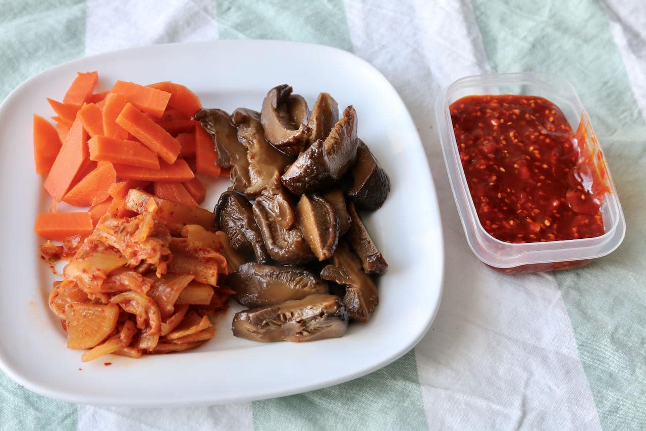 Ready to assemble homemade pork bibimbap with kimchi, marinated mushrooms, crunchy carrots and spicy sauce.