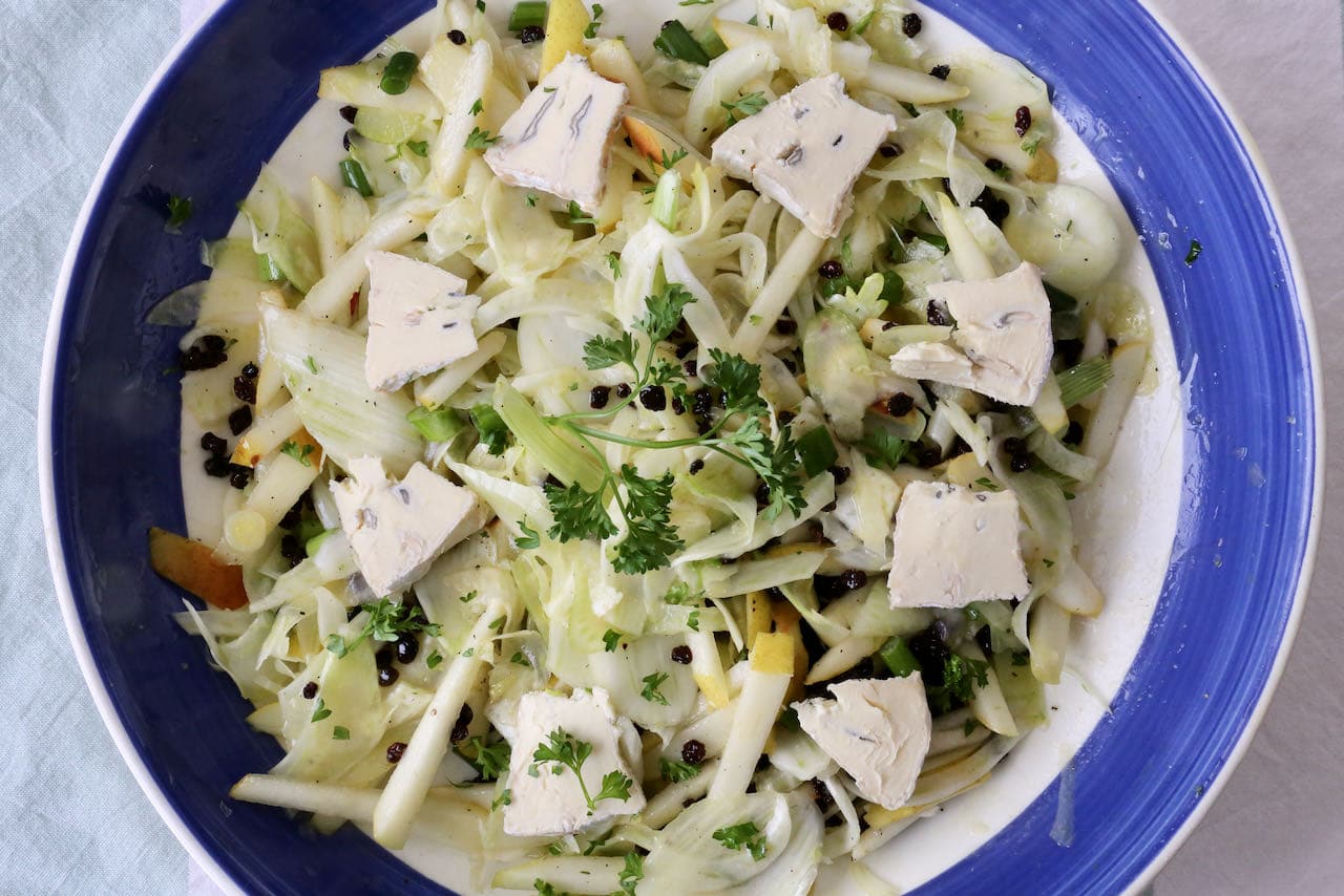 The best Pear and Fennel Salad is garnished with fresh parsley and sliced Cambozola cheese. 
