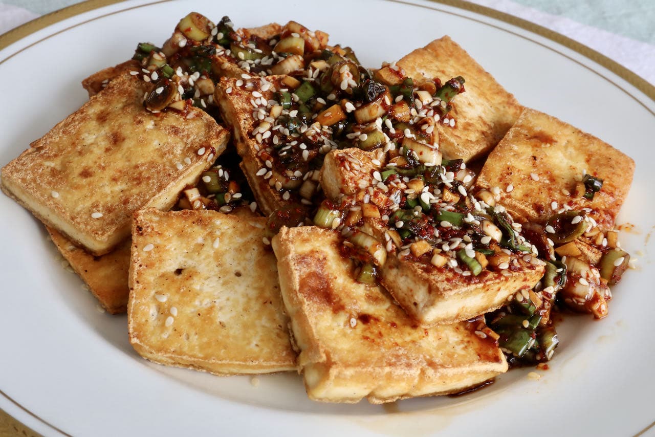 Serve slices of pan fried tofu topped with spicy Korean dressing and sesame seeds. 