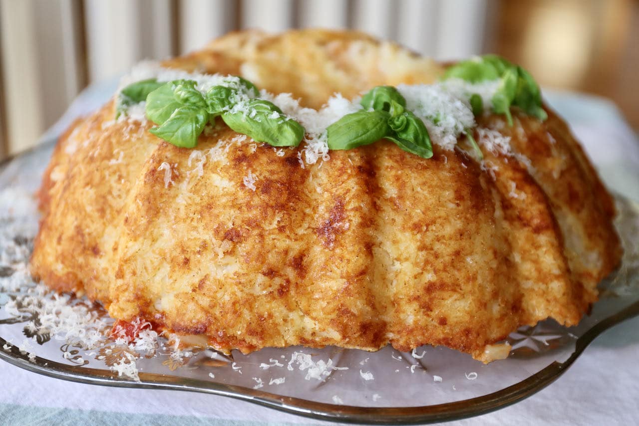 Serve Sartu Di Riso garnished with basil leaves and shredded parmesan cheese.