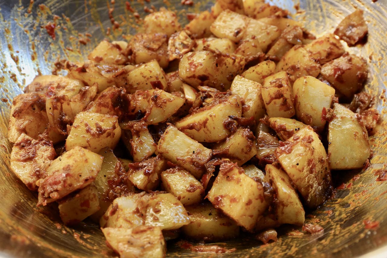 In a large mixing bowl toss potatoes with shallots, garlic and harissa until uniformly coated. 