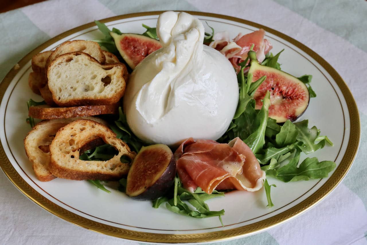 Serve Burrata and Prosciutto on a bed of arugula with crunchy crostini.