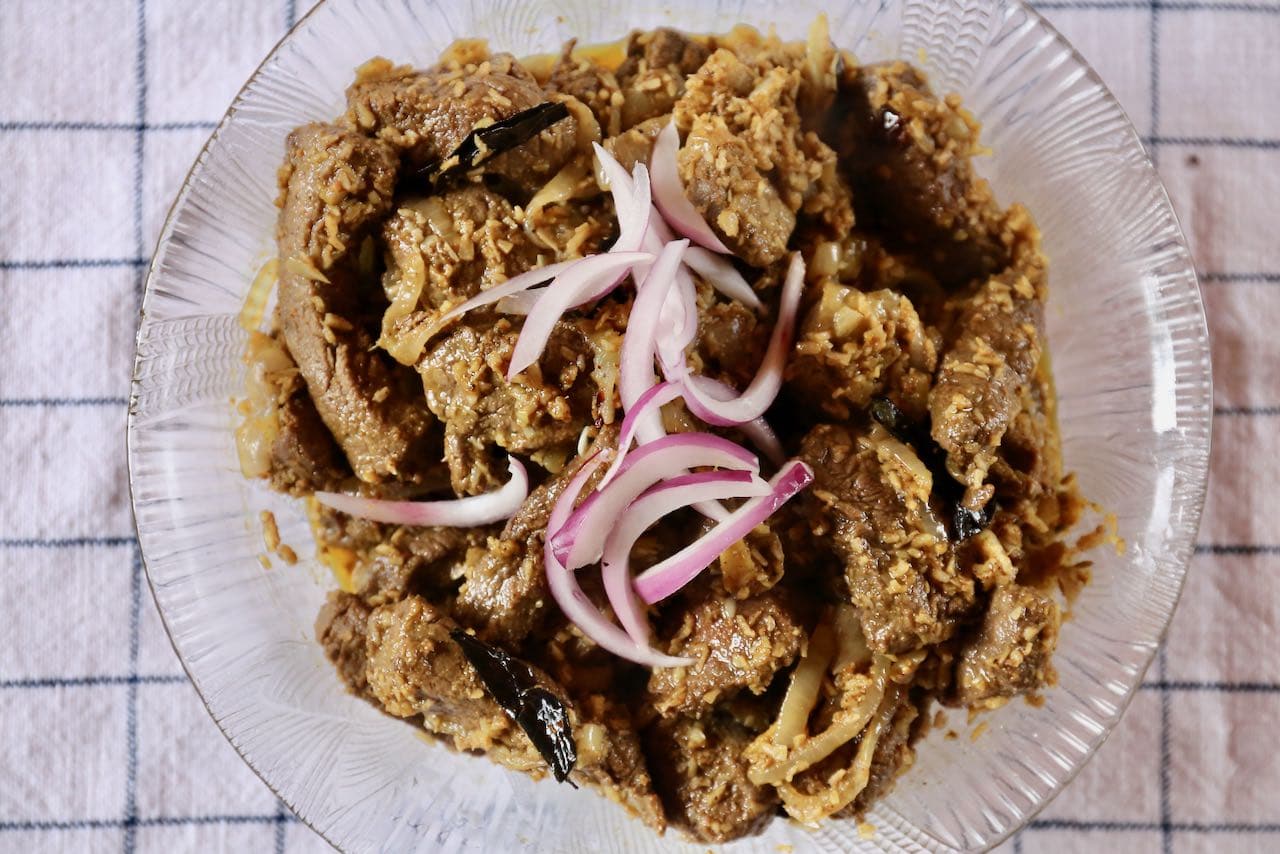 Serve Ularthiyathu Beef garnished with sliced red onion.