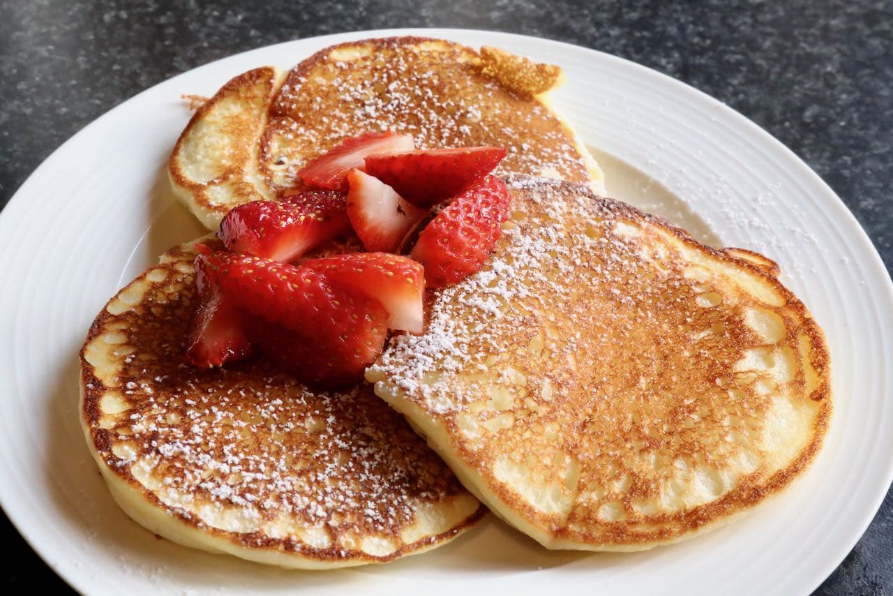 Serve Oladiki Pancakes at breakfast with icing sugar and fresh berries.