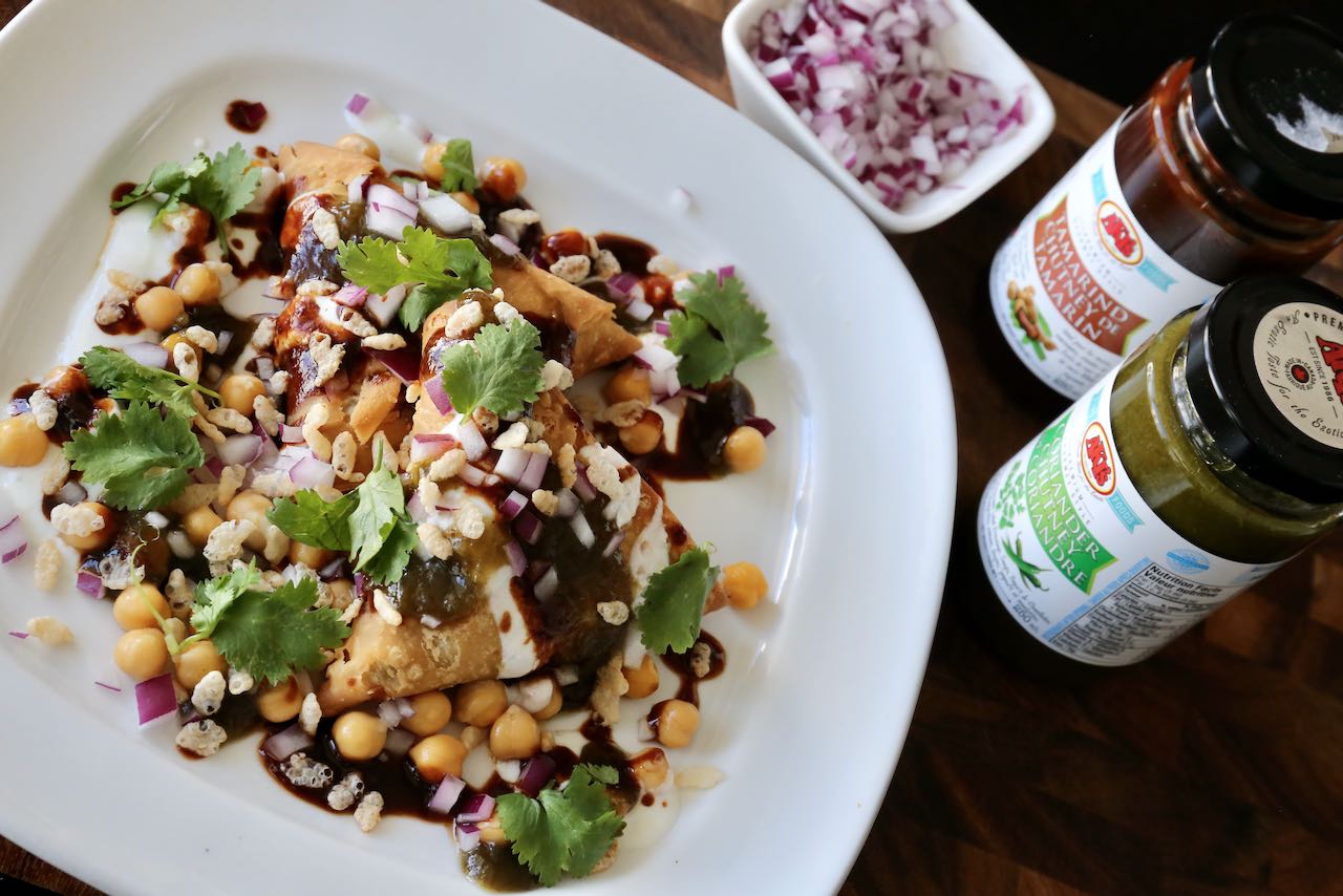 Drizzle Samosa Chaat with tamarind and cilantro chutney sauce.