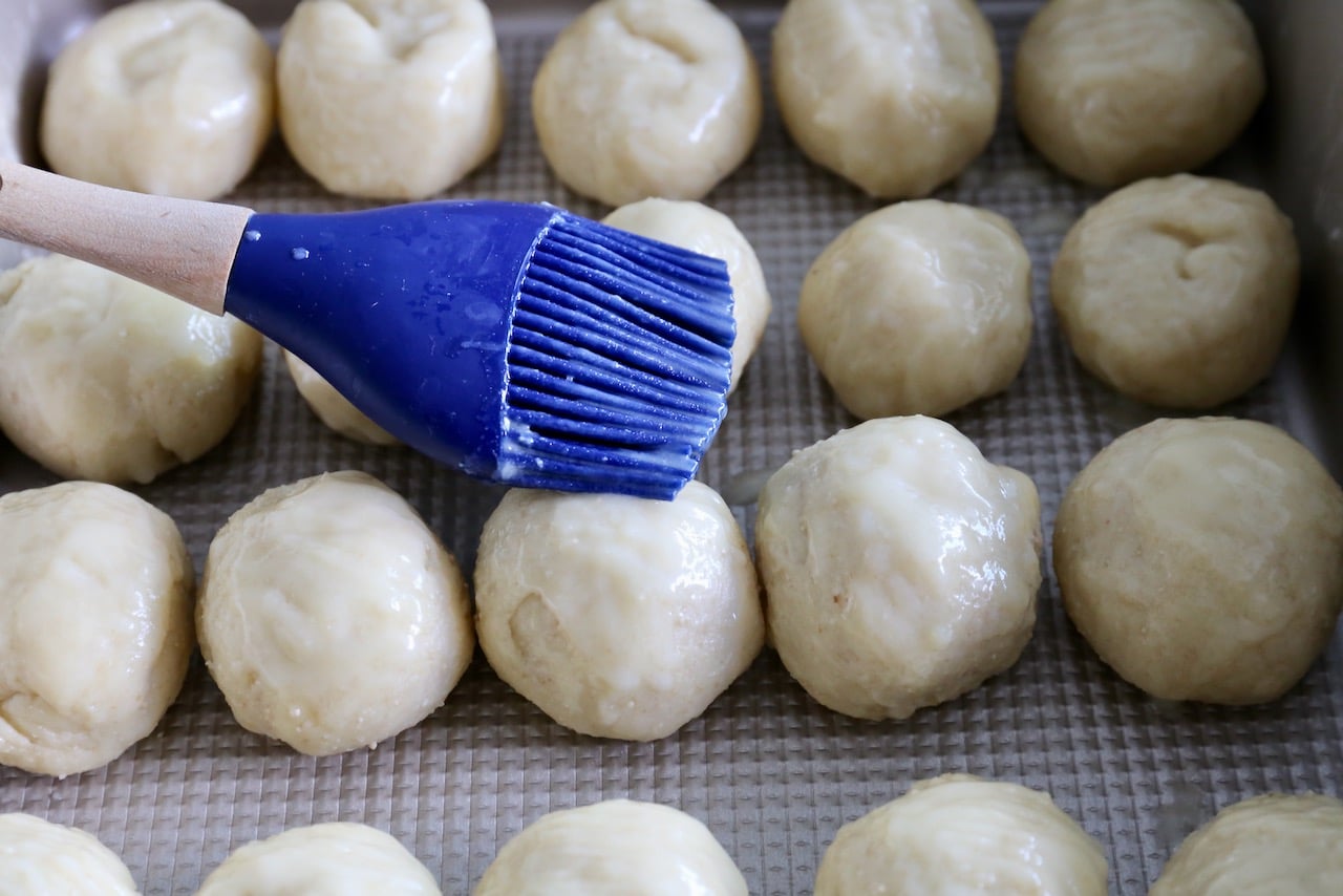 Brush Dukatove Buchticky dough balls in melted butter with a pastry brush before baking.