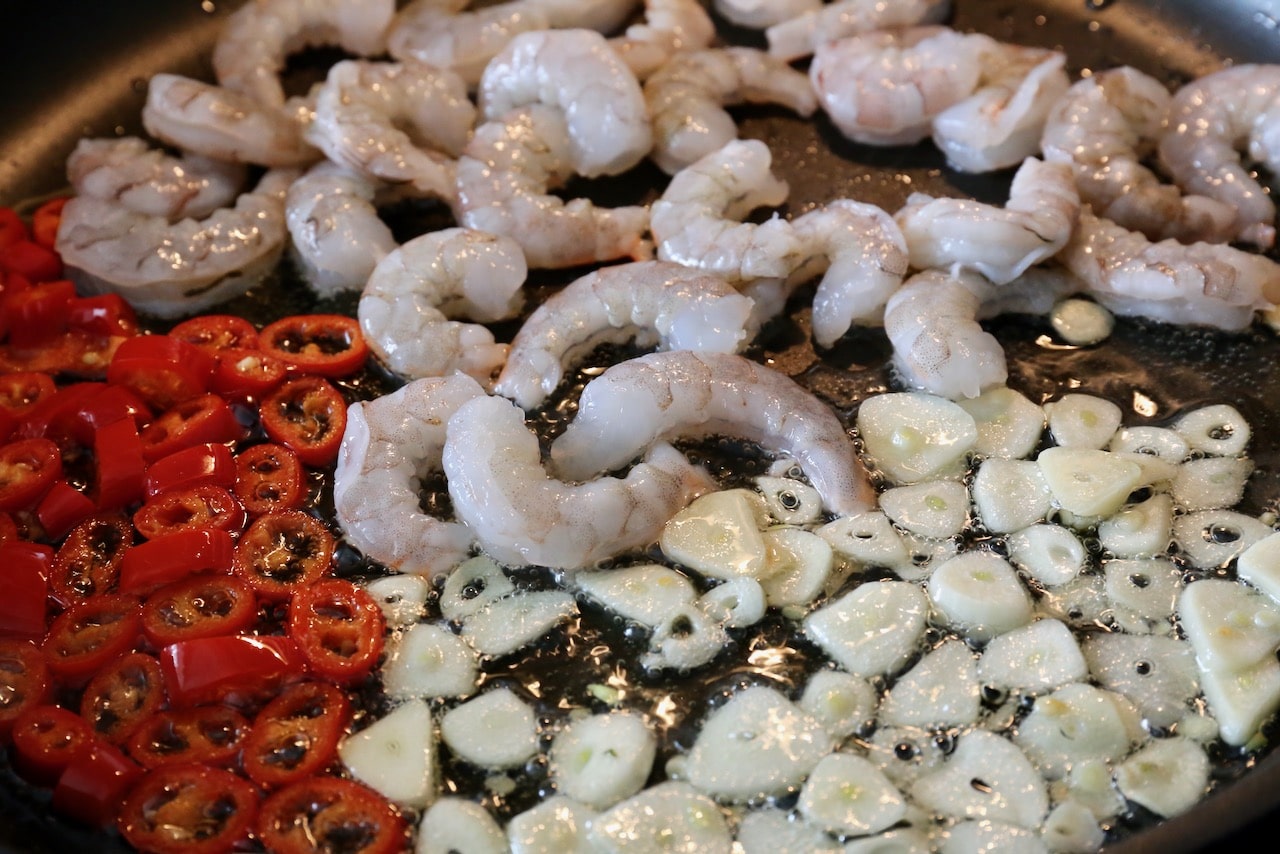 Spanish Prawns frying in a skillet featuring shrimp, garlic, and red chili.