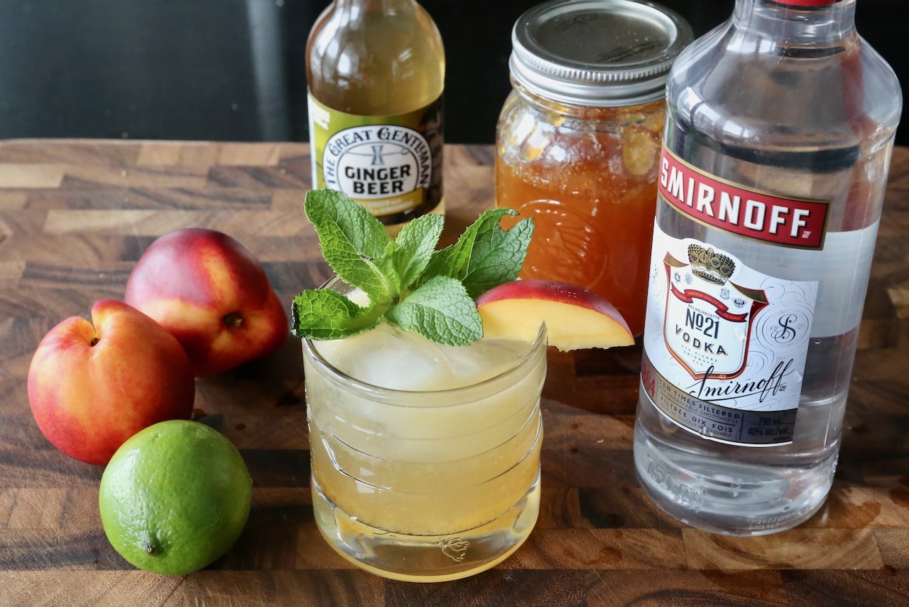 Garnish the summer cocktail with a fresh mint sprig and peach slice.