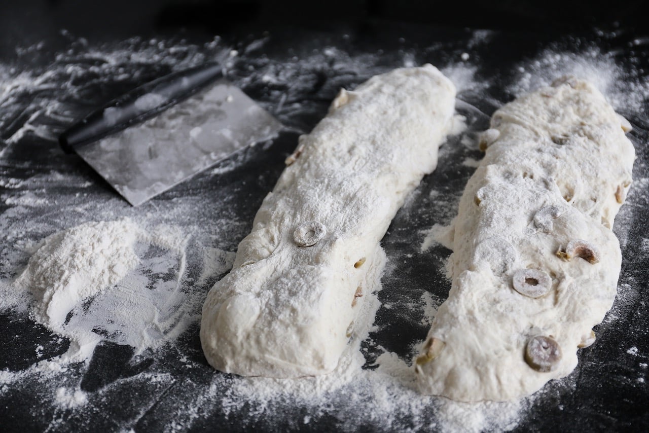 Use a bench scraper to separate the dough into 2 long pieces and form into ciabatta shape with your hands.