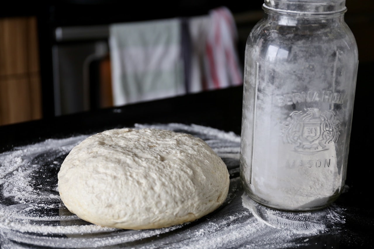 Proof our easy homemade pizza dough then cut in two and roll out onto flour dusted counter.