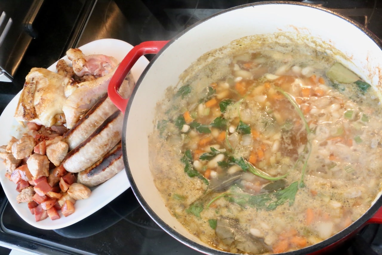 After browning the meats, simmer broth, vegetables, beans and herbs in a large Dutch Oven.